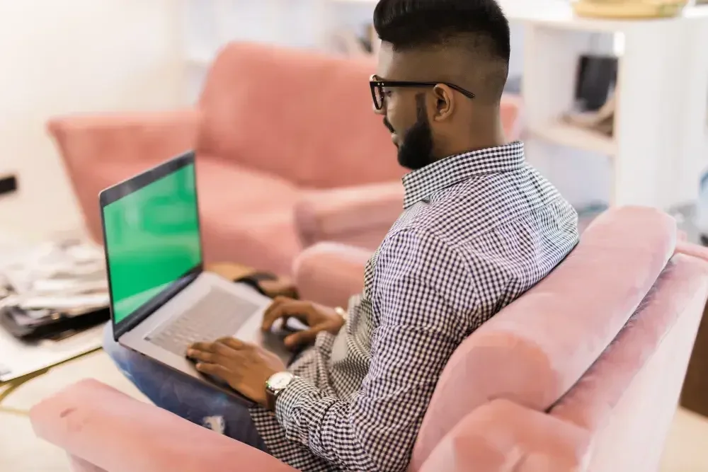 The owner of an LLC works on his laptop and sits in a comfy chair in his home.