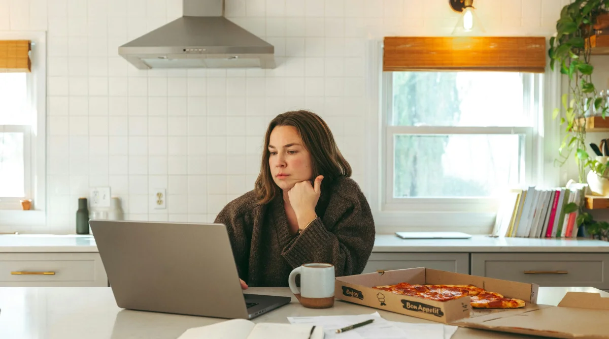 Woman working on a laptop in a kitchen with pizza