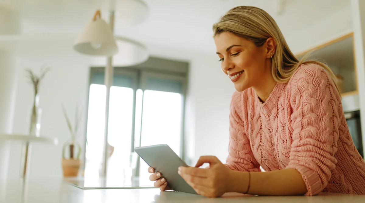 Smiling woman in pink sweater holding a tablet