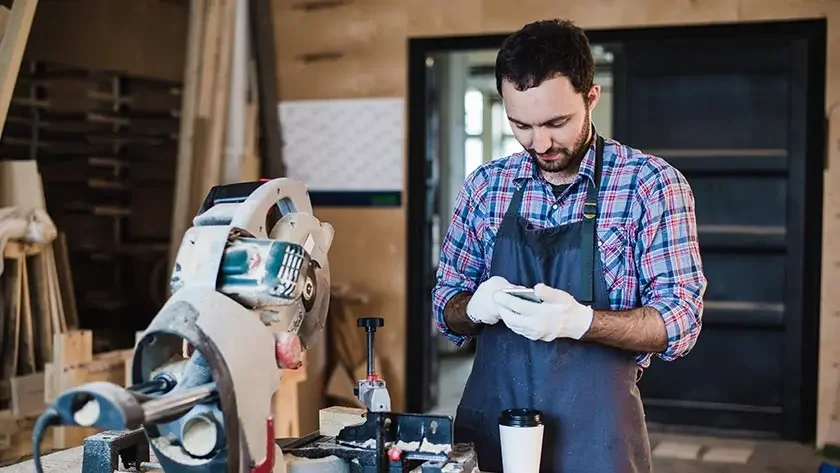 A small business owner uses a calculator as he works in his woodshop.