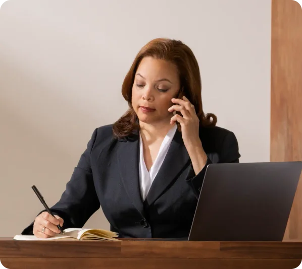 woman sitting at her desk making a call and taking notes.