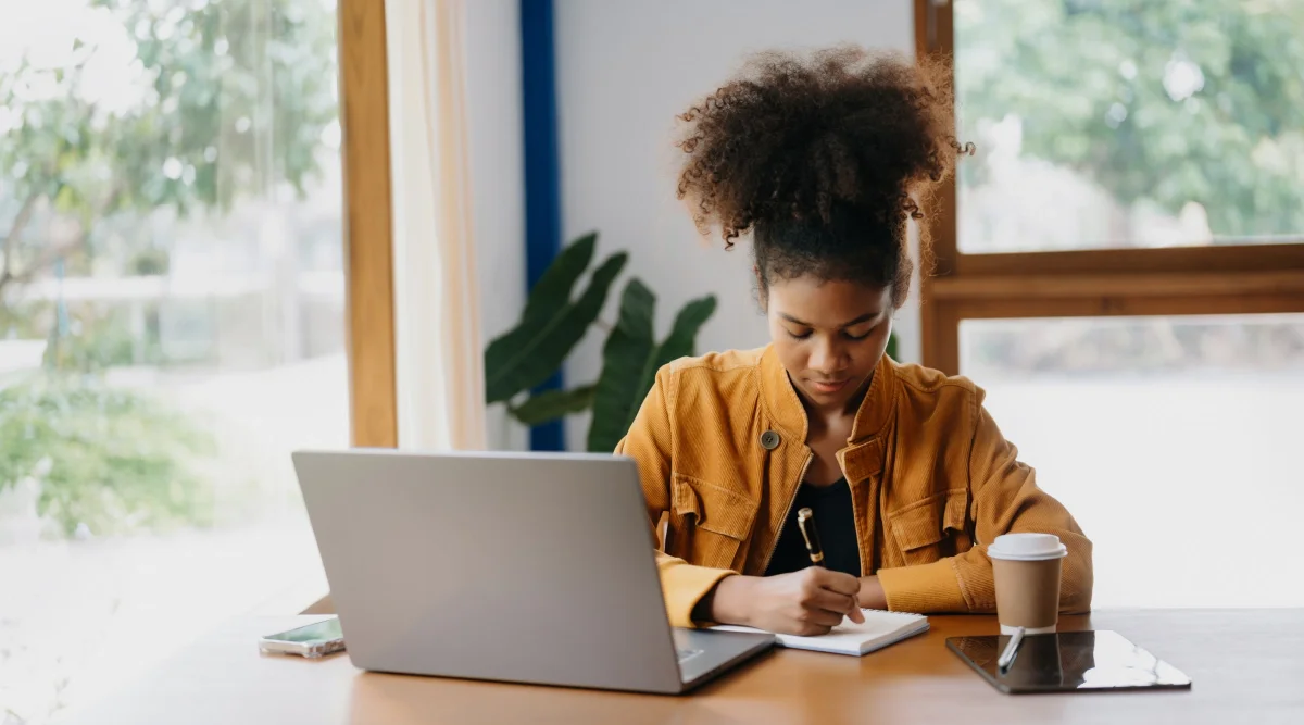 Woman writing notes with laptop on table