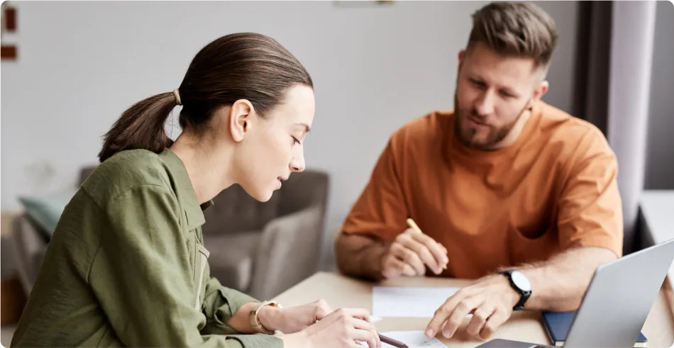 Brunette white woman with her hair in a pony tail wearing a long sleeved green blouse sitting next to a brunette White man wearing a orange shirt sitting in front of a laptop discussing their LegalZoom business dissolution.