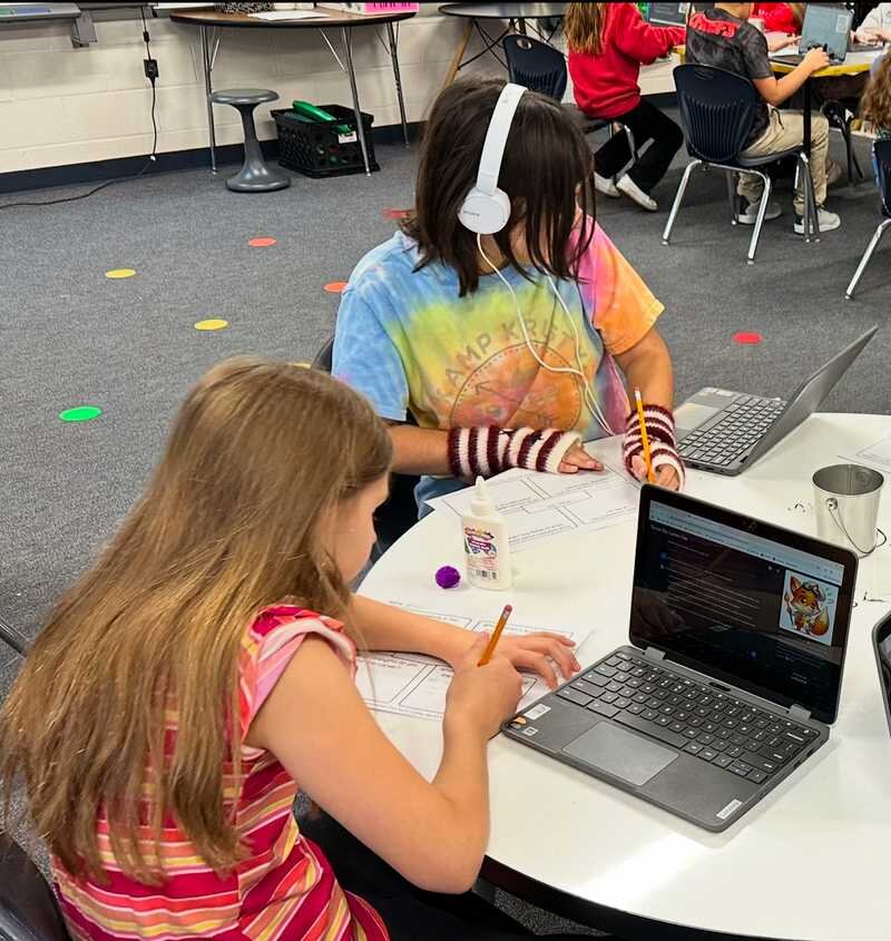 Students sitting at a table working on laptops.