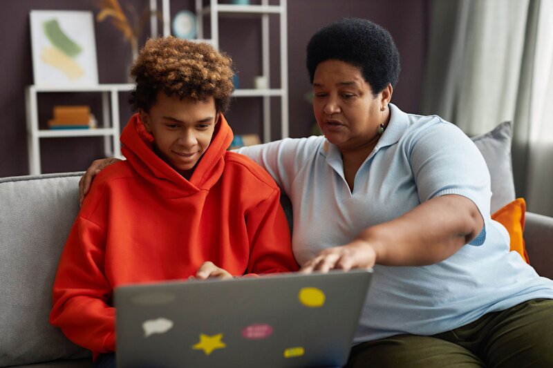 A son and mother are working together at a laptop.