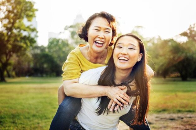 A mother riding piggy-back on her daughter. They are both smiling. 