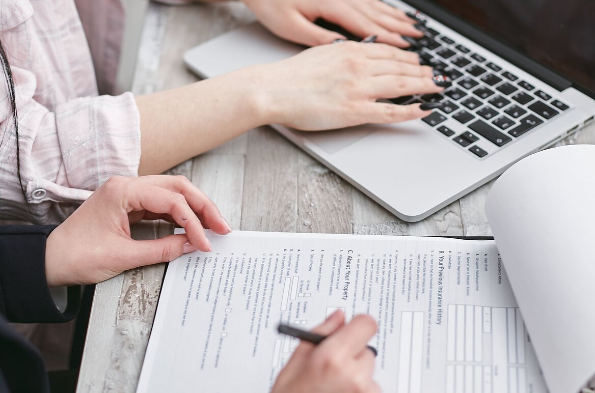 Person reviewing a financial statement with a calculator and laptop on a wooden desk