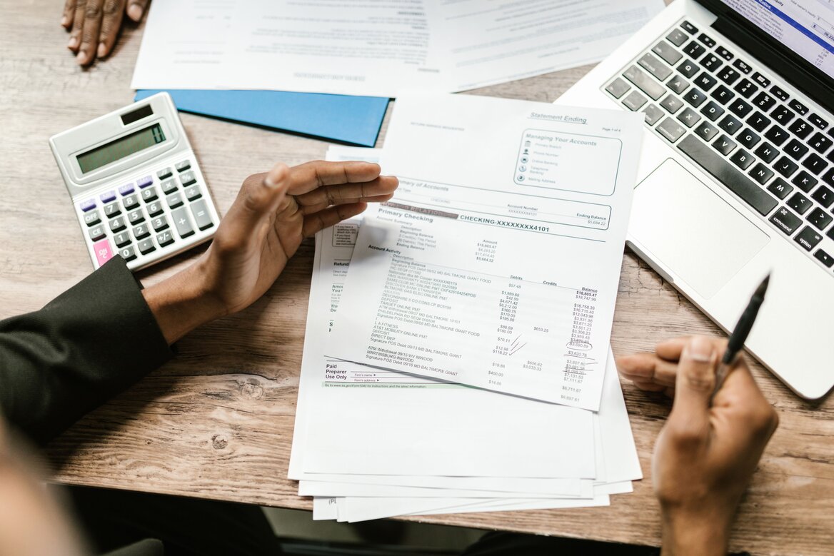 A person reviewing financial statements and income records with a calculator and laptop