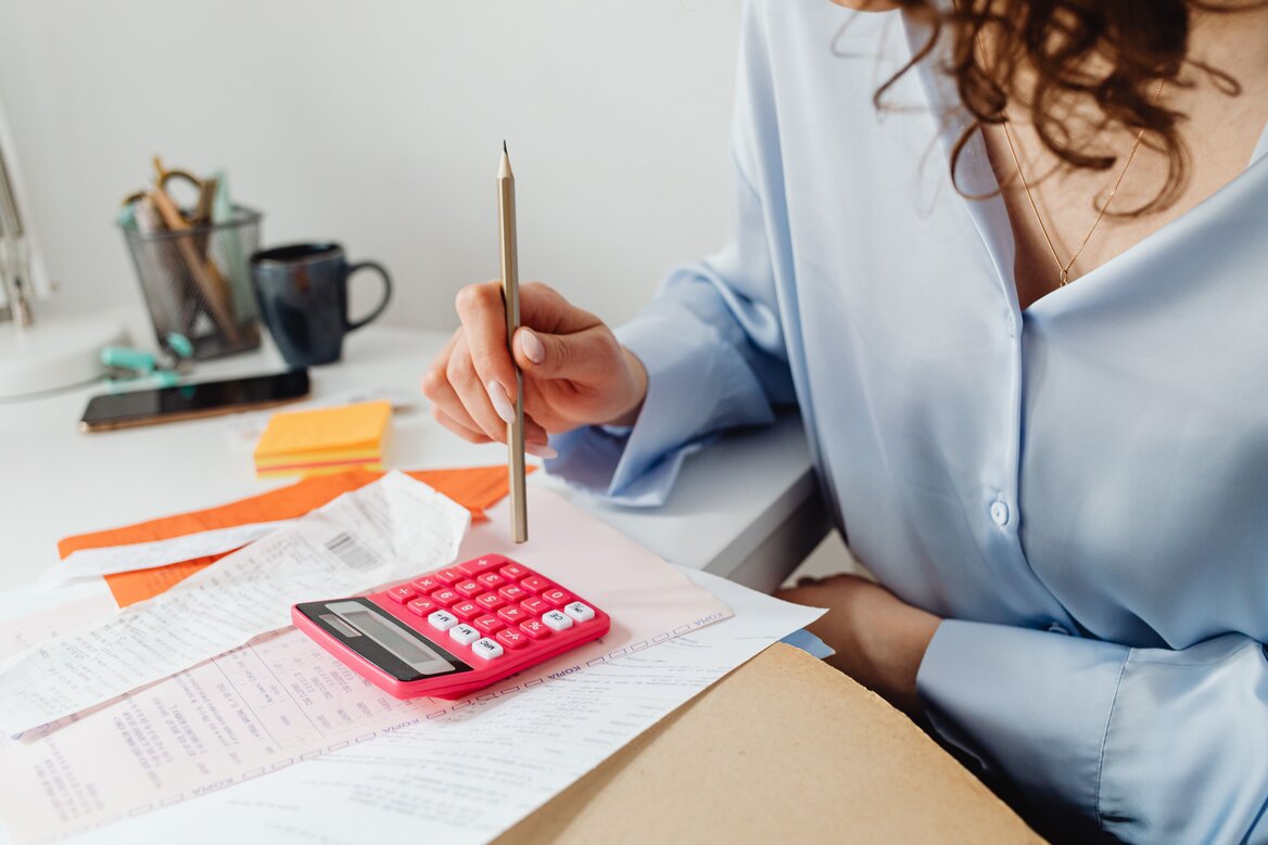Woman calculating expenses using a calculator, receipts, and paperwork at her desk"