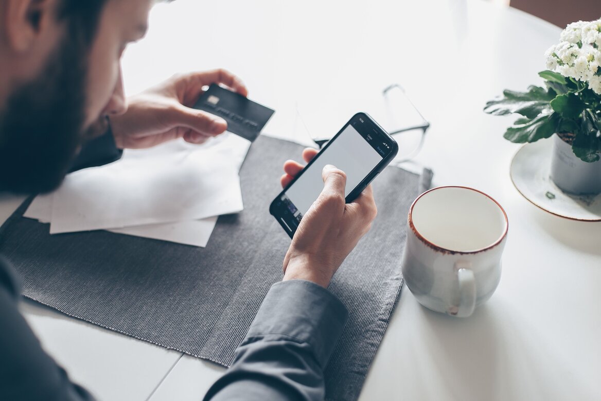  A person tracking business expenses on a mobile app with a bank card and receipts on the desk