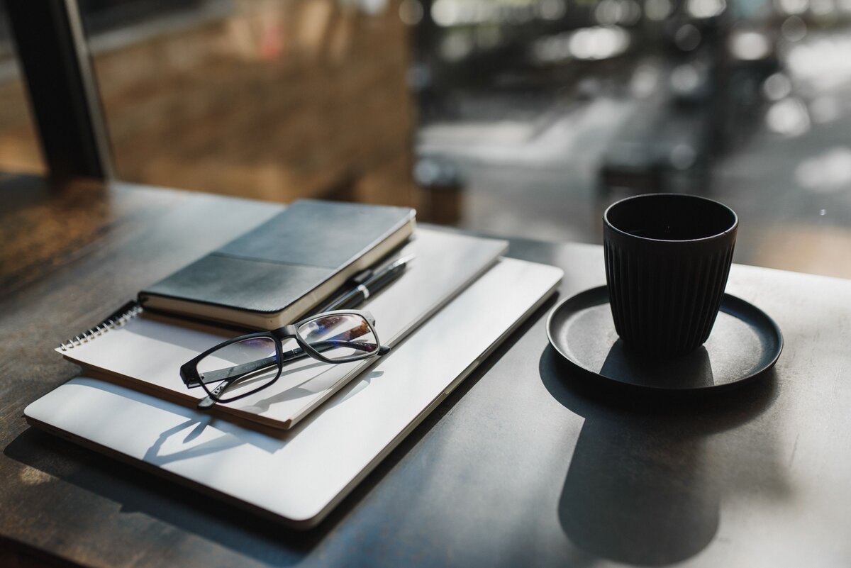 A minimalist desk featuring eyeglasses, a planner, and a notebook reflects the clarity self-employed professionals need to plan their start date based on their income