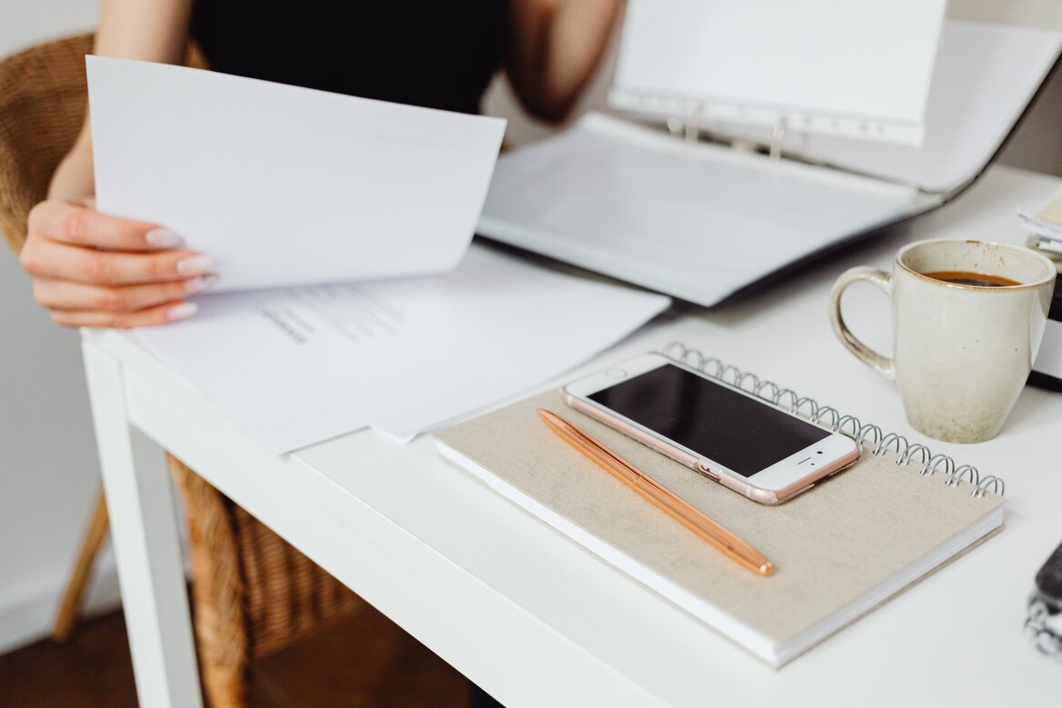 Freelancer reviewing paperwork at a tidy home office desk with a phone and notebook