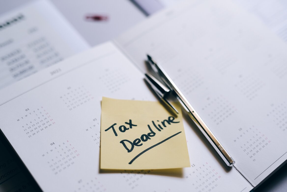 A sticky note reading "Tax Deadline" placed on a calendar with a pen