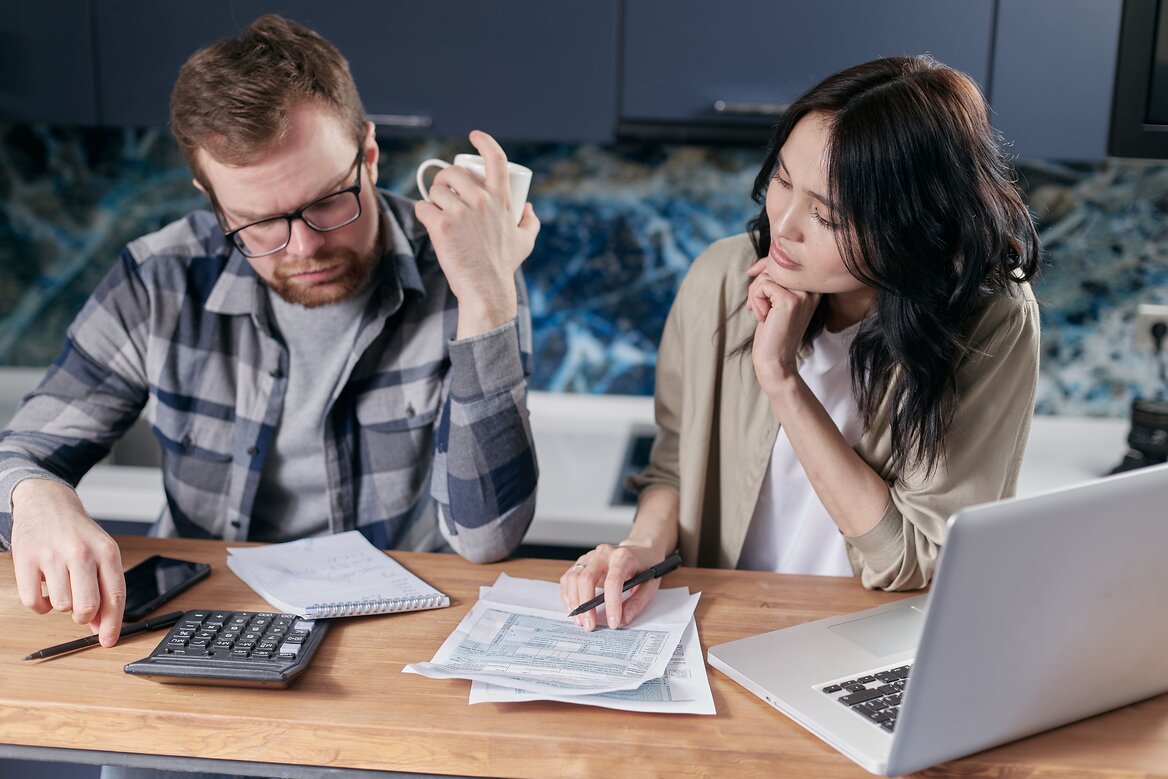 Two people reviewing tax documents and using a calculator at a kitchen table

