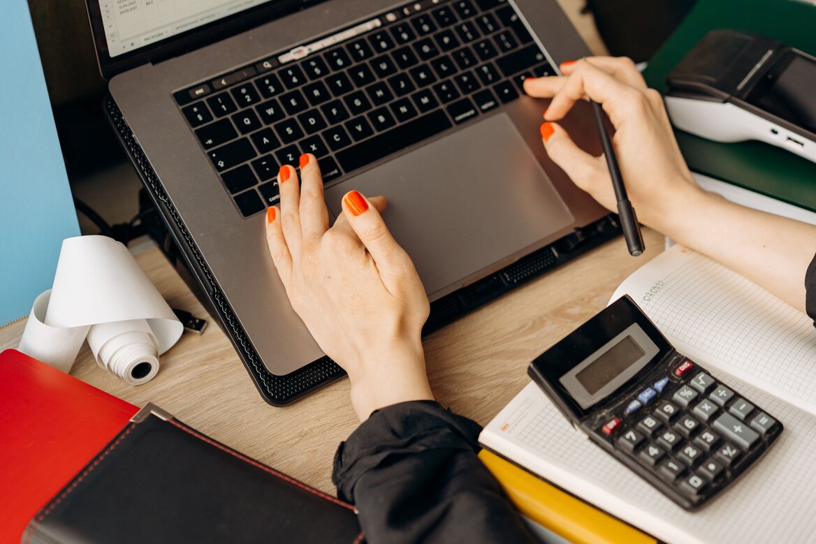 : Hands typing on a laptop with a calculator and notebook on the desk, representing accounting software in use