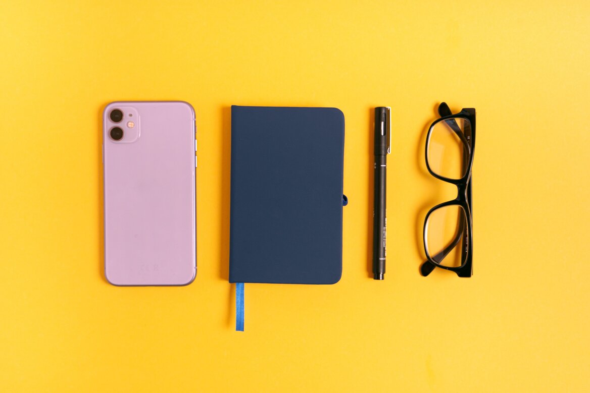 Flat lay of phone, notebook, pen and glasses representing everyday self-employed business expenses