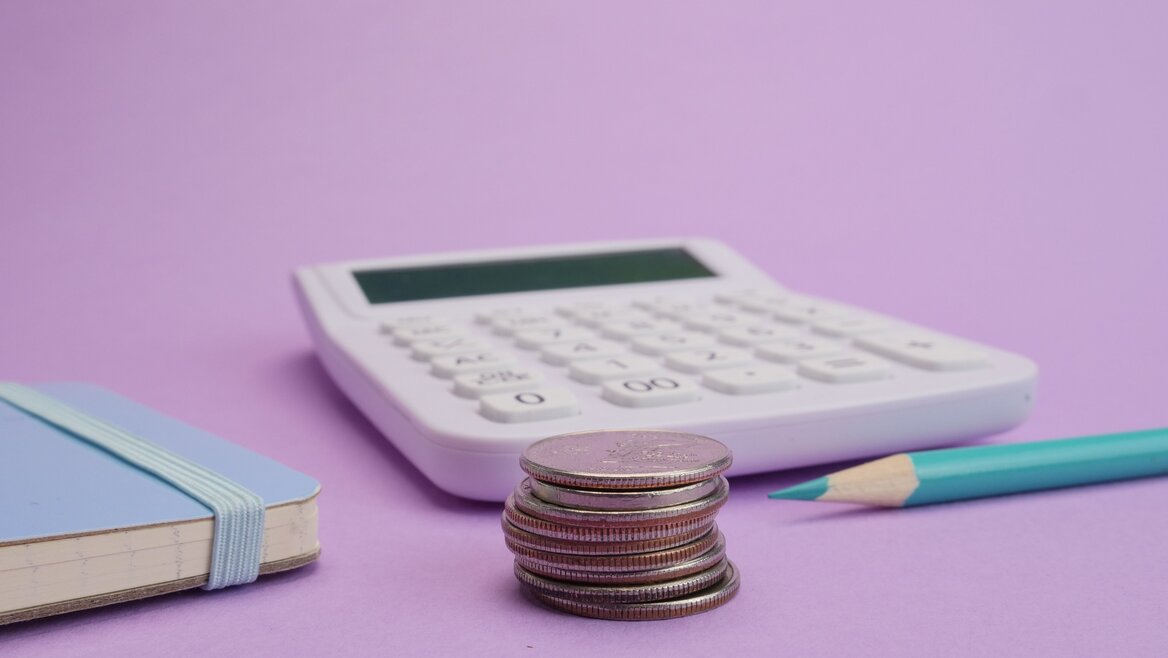 A calculator, stacked coins and an open notebook on a desk, illustrating dividend tax calculations and record-keeping for UK Self Assessment filers.