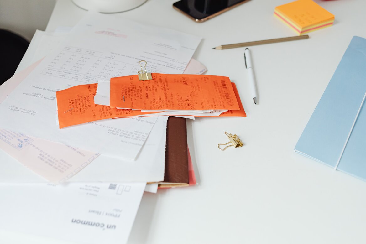 Disorganised pile of receipts and financial documents on a white desk