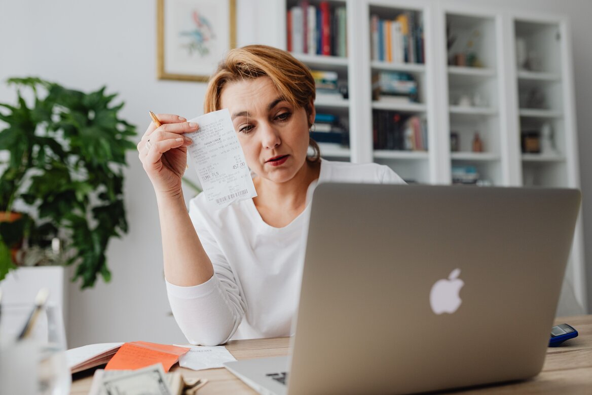 Close-up of a person reviewing tax documents and entering information on a laptop.