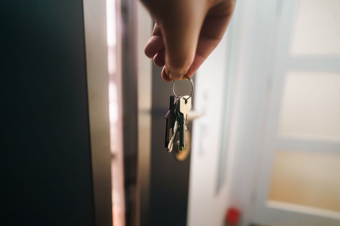 A hand holding a set of house keys outside a front door