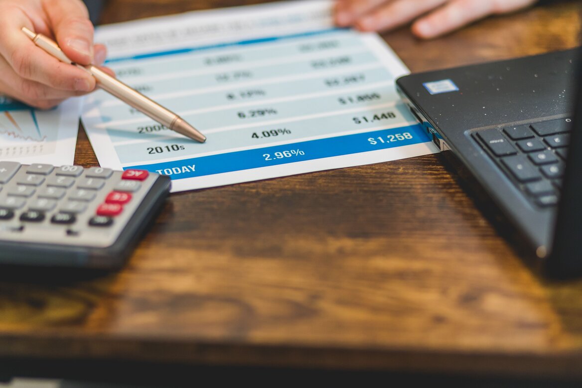 Close-up of hands reviewing a printed financial report with a calculator and laptop nearby