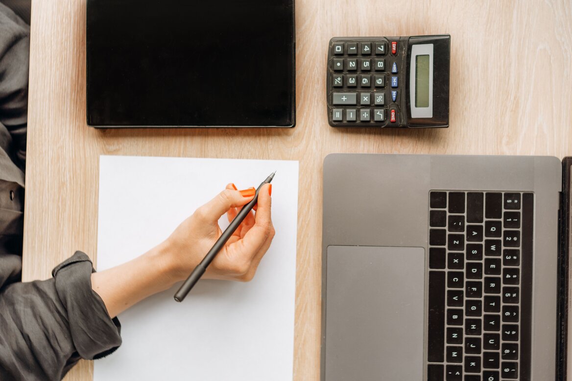 Overhead view of a desk with a laptop, calculator, and notepad, representing contractor bookkeeping