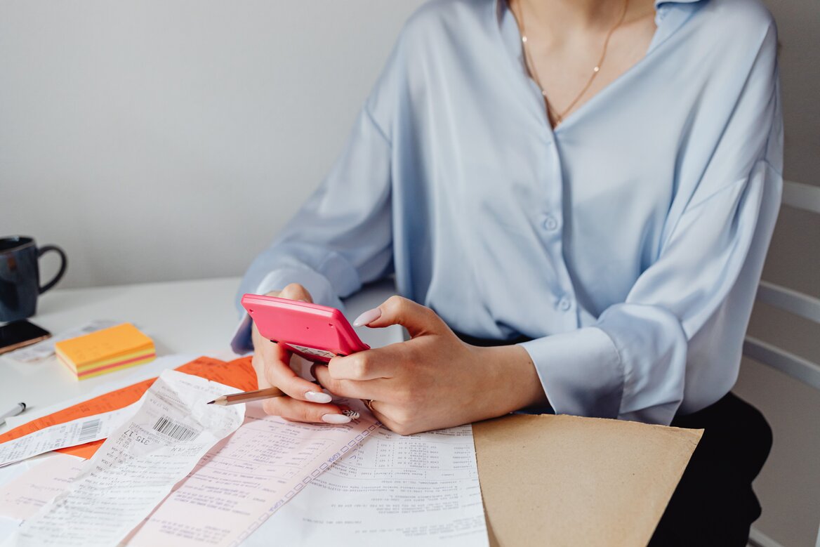 Self-employed woman using a calculator to organise receipts and tax paperwork on a desk