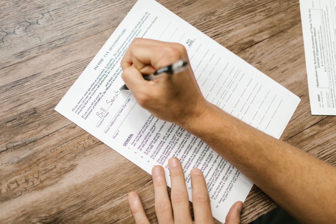  Close-up of a hand writing on an income tax questionnaire form with a pen