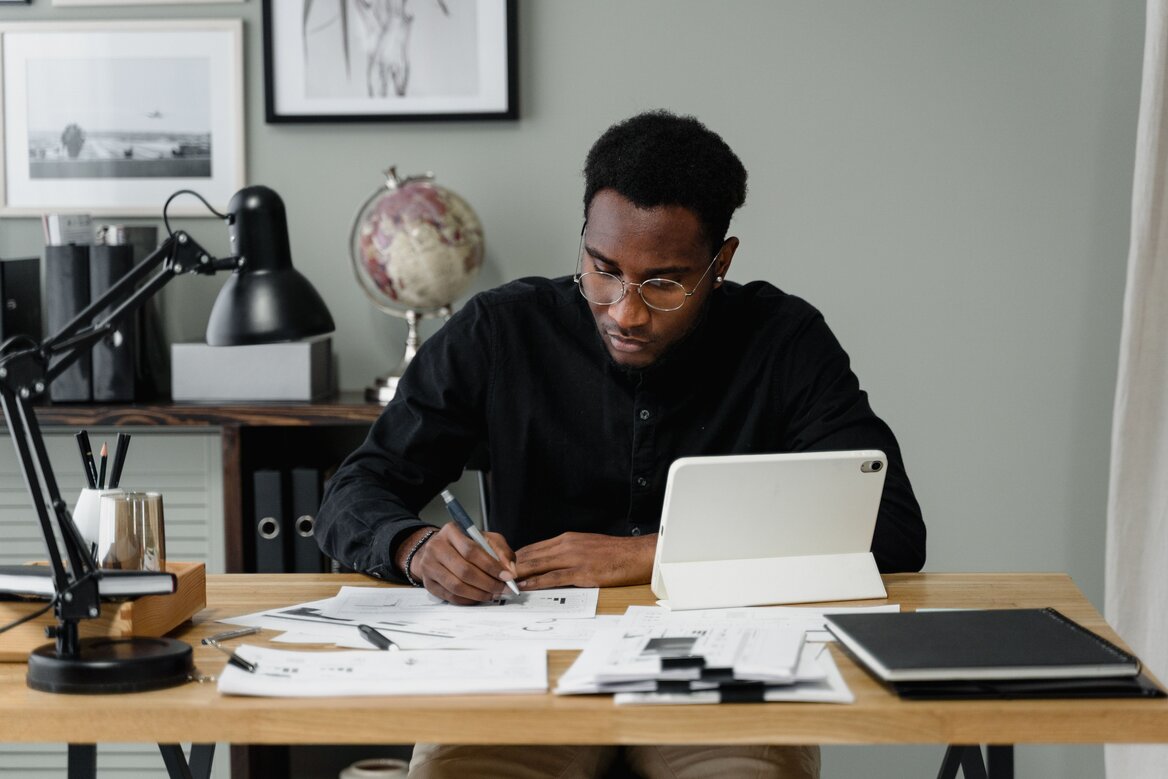 Sole trader reviewing self-assessment documents at a home office desk with a tablet and paperwork