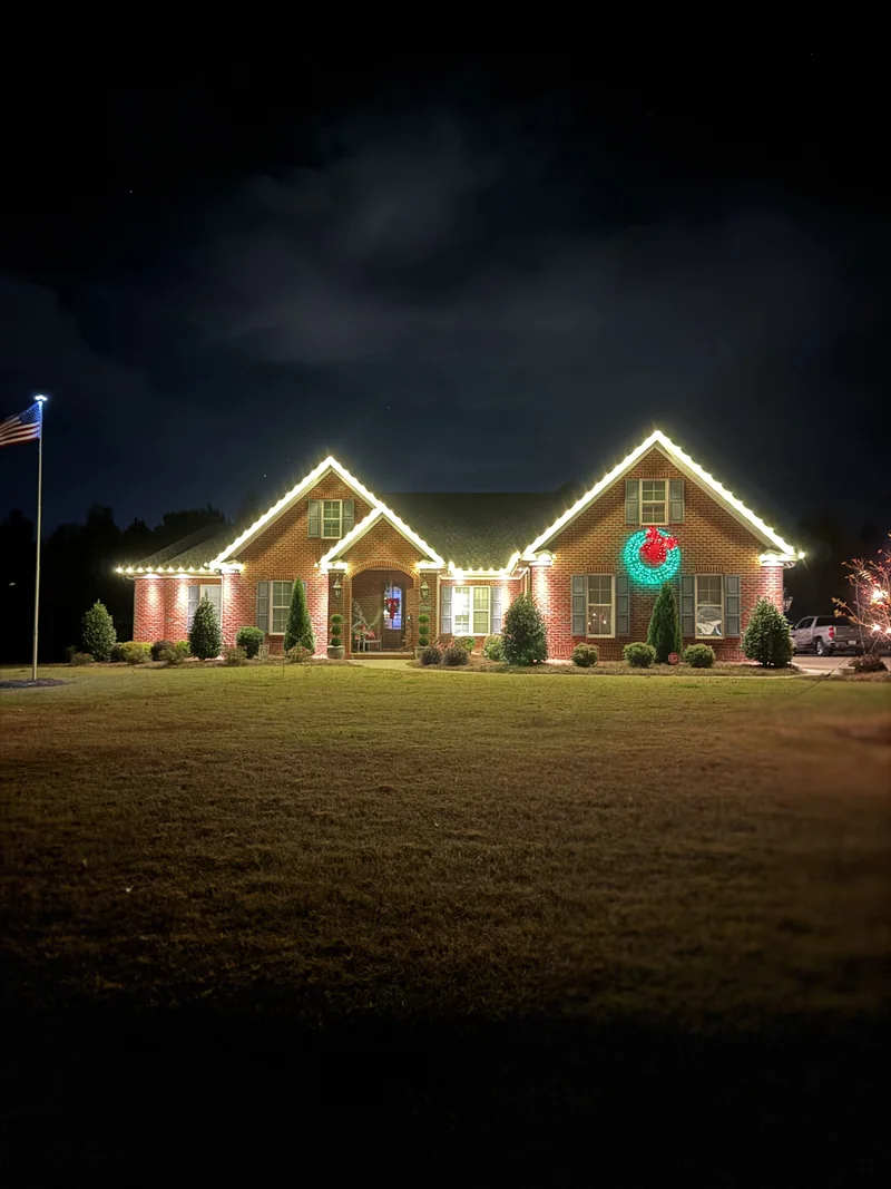 Brick home outlined with warm holiday lights and a glowing wreath at night