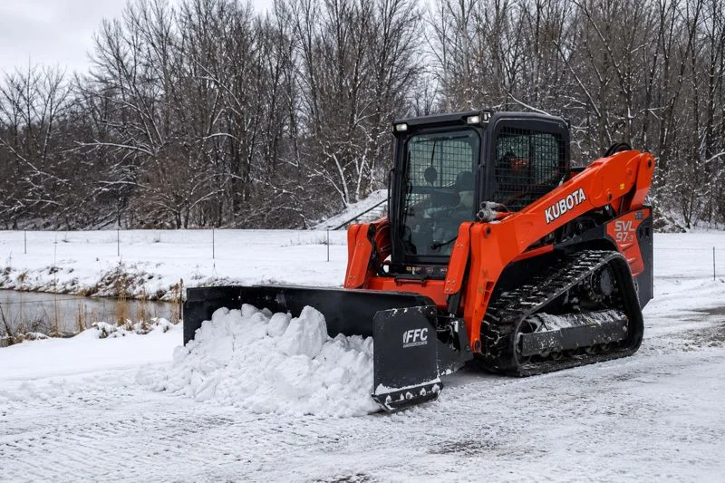 Kubota track loader clearing snow from a paved property in winter