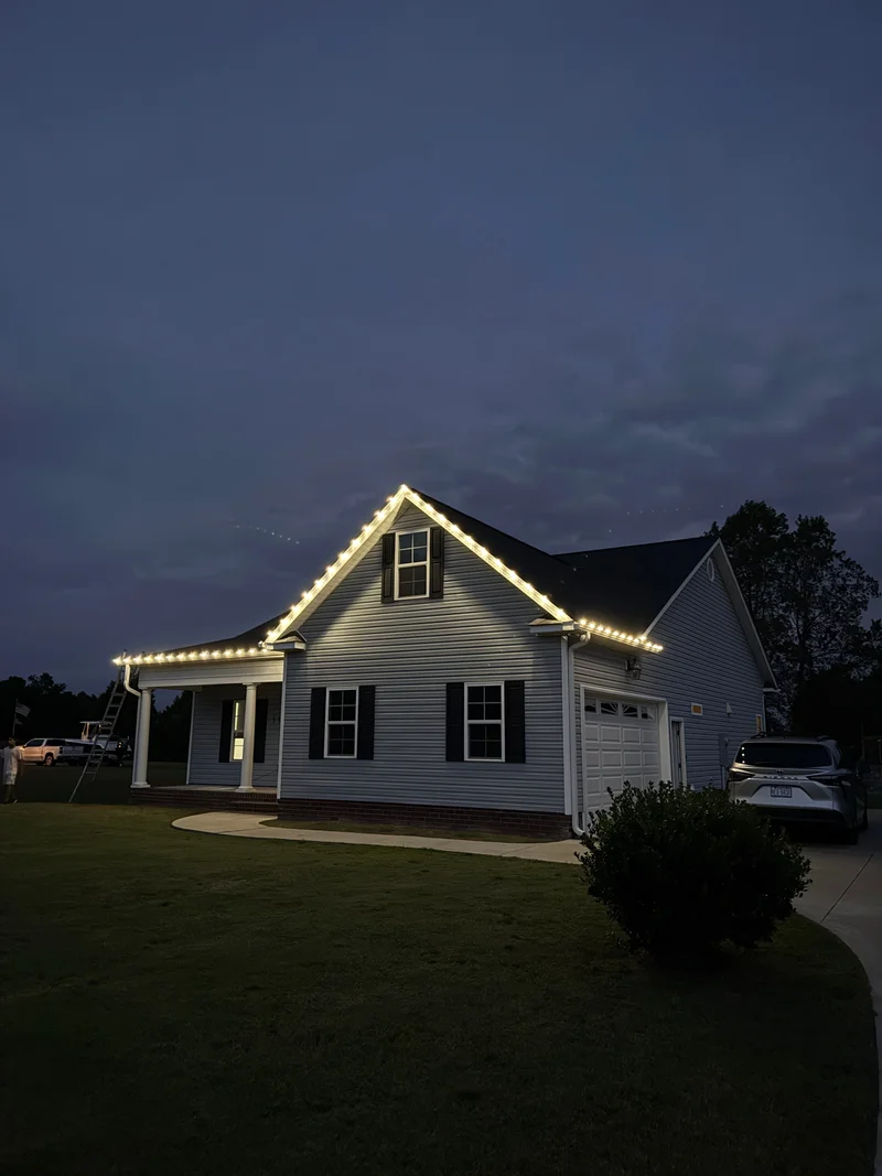 Warm roofline lights outlining a blue home at dusk