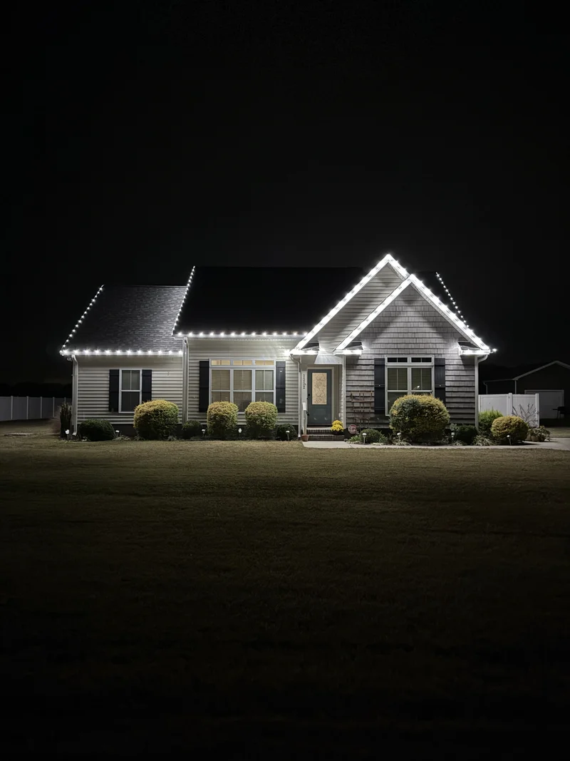 A single-story home with warm Christmas lights across the roofline at night
