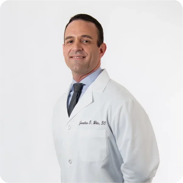 Doctor in a white coat smiling against a plain background.