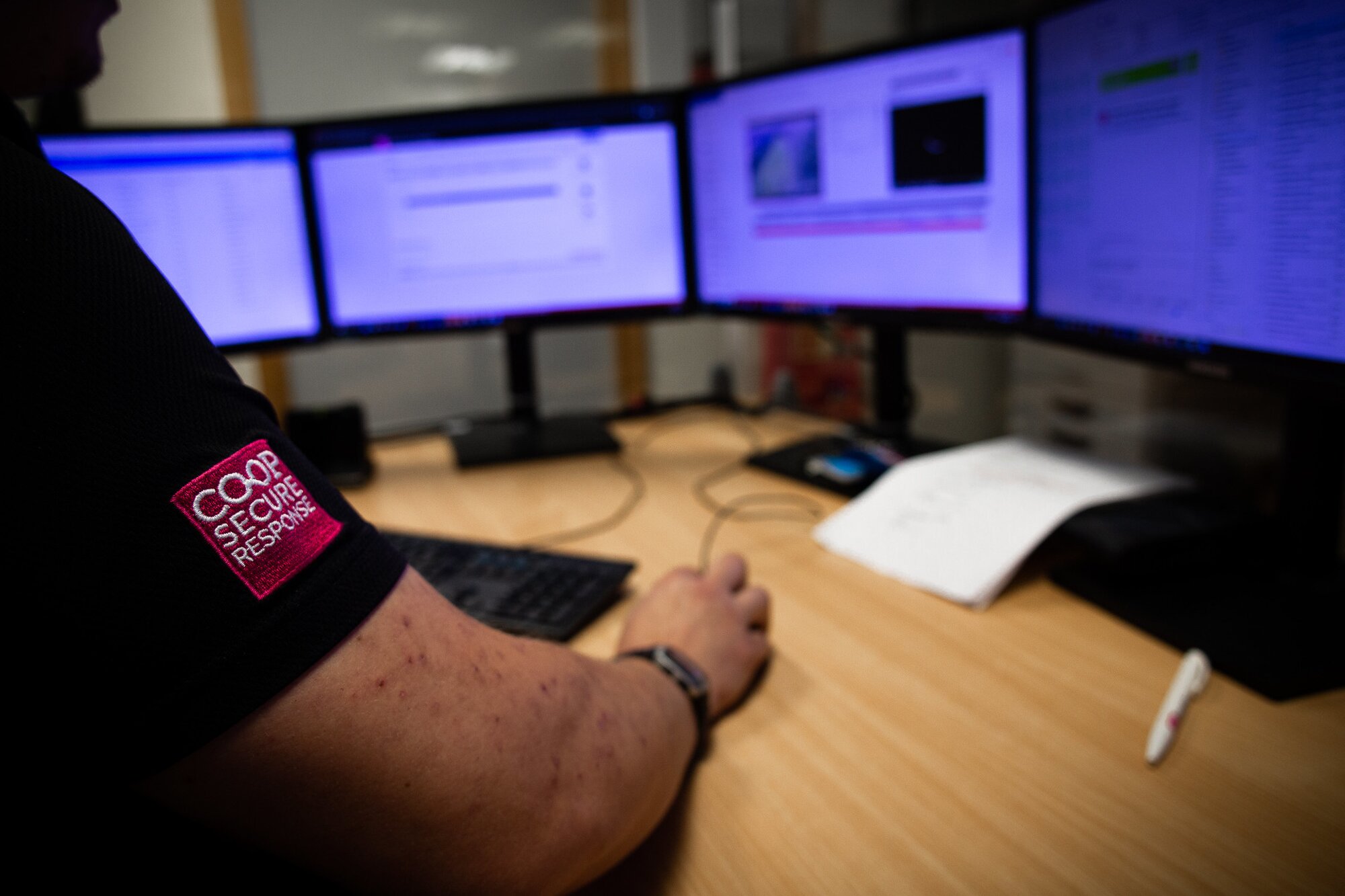 Co-op Secure Response security operator monitoring fire alarm systems on multiple computer screens.