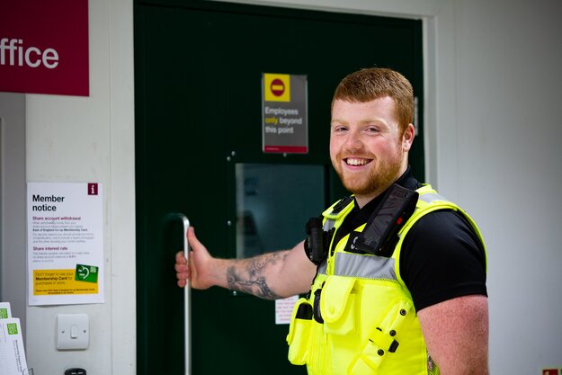 East of England Co-op security team member smiling in high-visibility uniform during work.