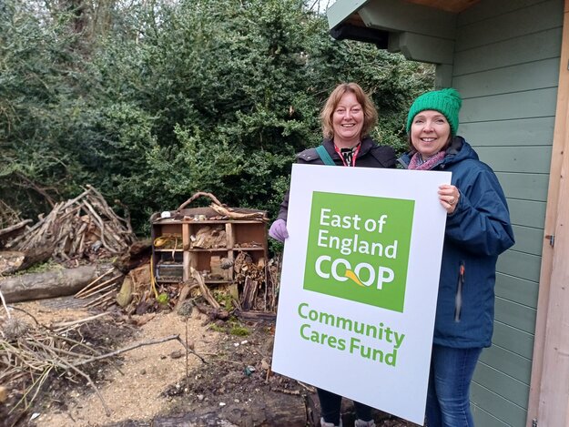 Community members holding East of England Co-op Community Cares Fund sign, supporting local initiatives.
