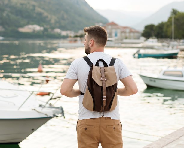 Man with a backpack standing looking out onto the water docked with boats.