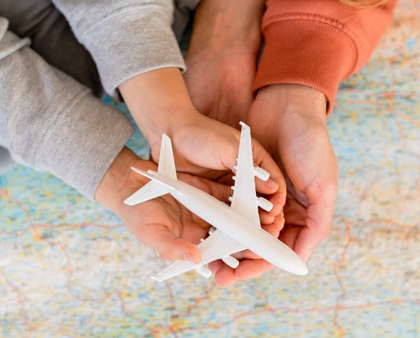 A family of three, hands placed on top of each other holding a white model airplane above a map of the world.