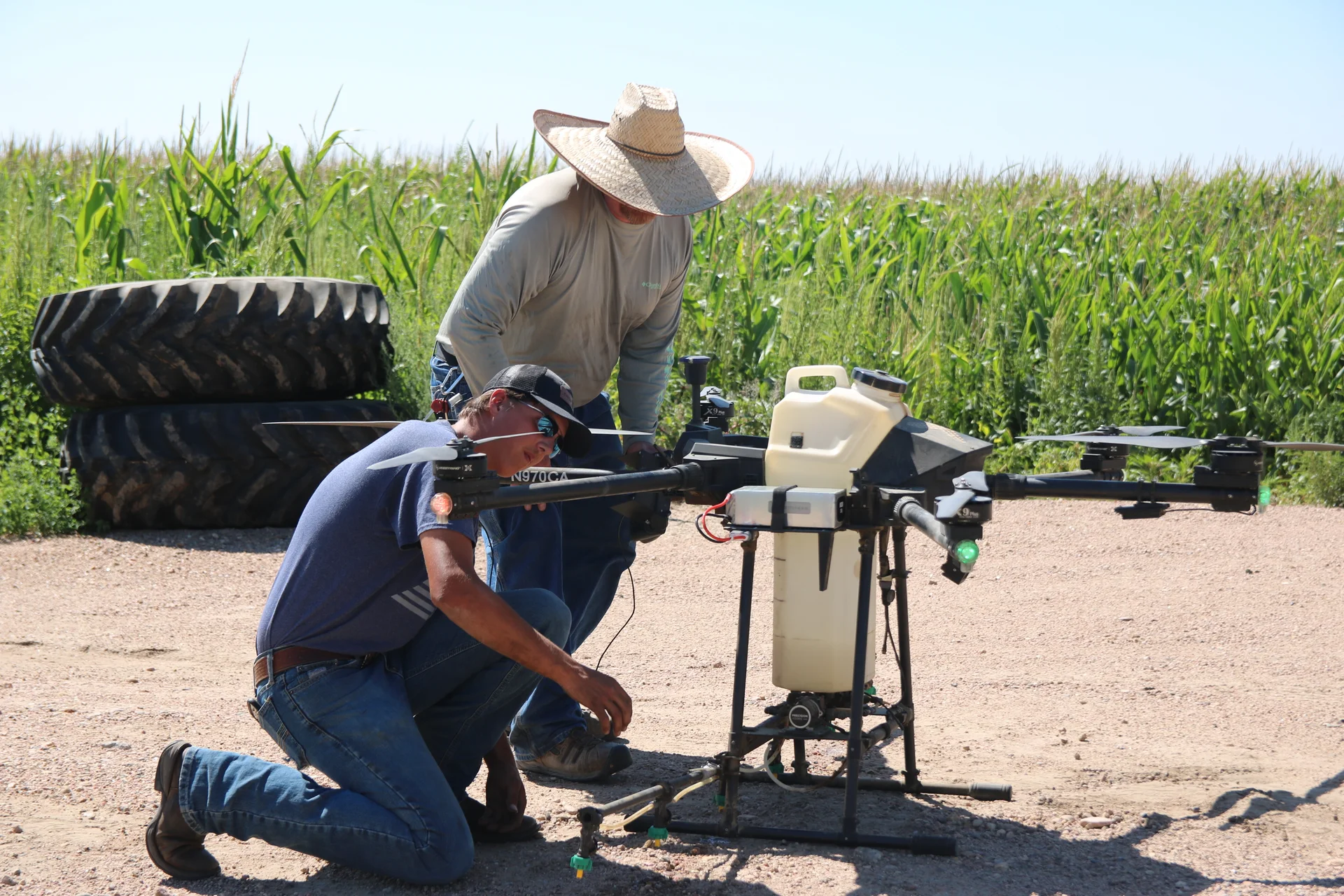 Nineteen-year-old Preston Weichel (left) kneels down to inspect the drone before Joseph Daviss (right) flies it. Their current drone is seven feet tall and carries about 40 pounds, but the drone that Crop Air is in the process of getting will carry about 100 pounds, Daviss said. Photo: Emma VandenEinde, KUNC. 