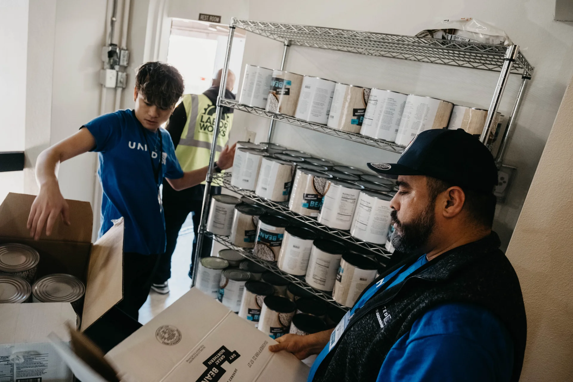 United Airlines employees Ryota (left) and Fernando (right) open packages of beans. Many companies will come to the center for volunteer hours. Photo: Peter Vo, Rocky Mountain PBS