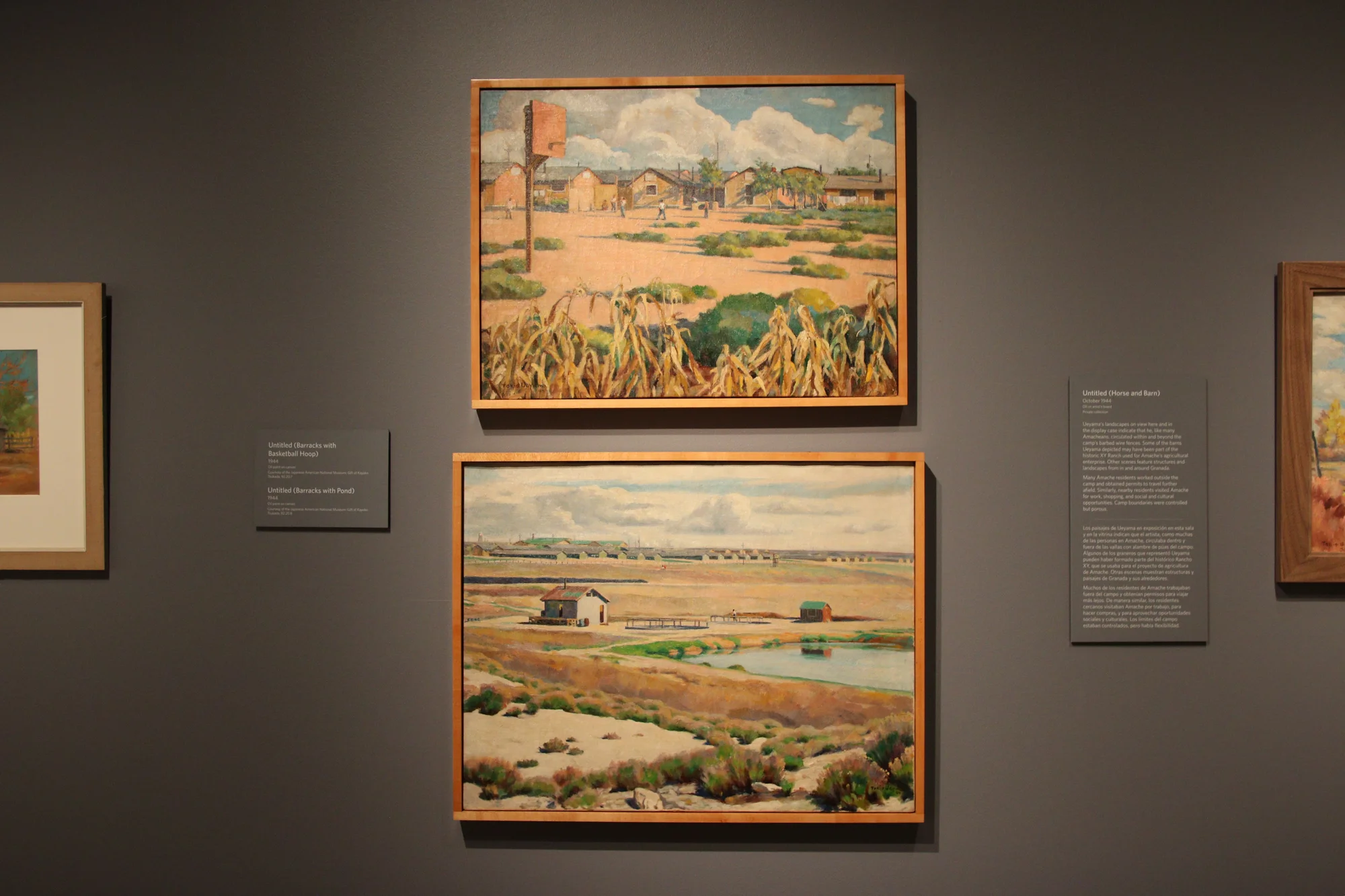 Some of Ueyama's paintings in the exhibit show scenes of Amache during his incarceration. The top has a camp view of the barracks with people playing baseball. There is a basketball hoop that is made from found materials. Below that is a landscape from outside of Amache with barbed wire fences and one of the armed guard towers in the middle background. Photo: Emma VandenEinde,KUNC