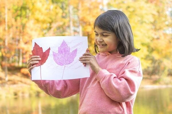 Child holding a drawing of fall leaves