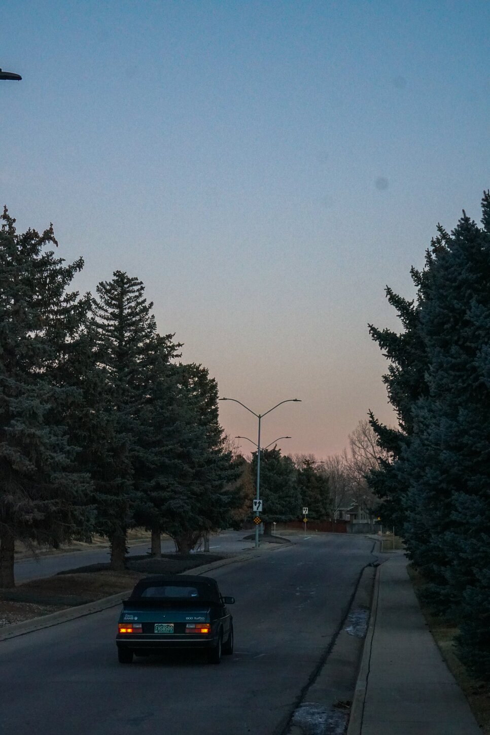 a green convertable saab drives down a road after sunset