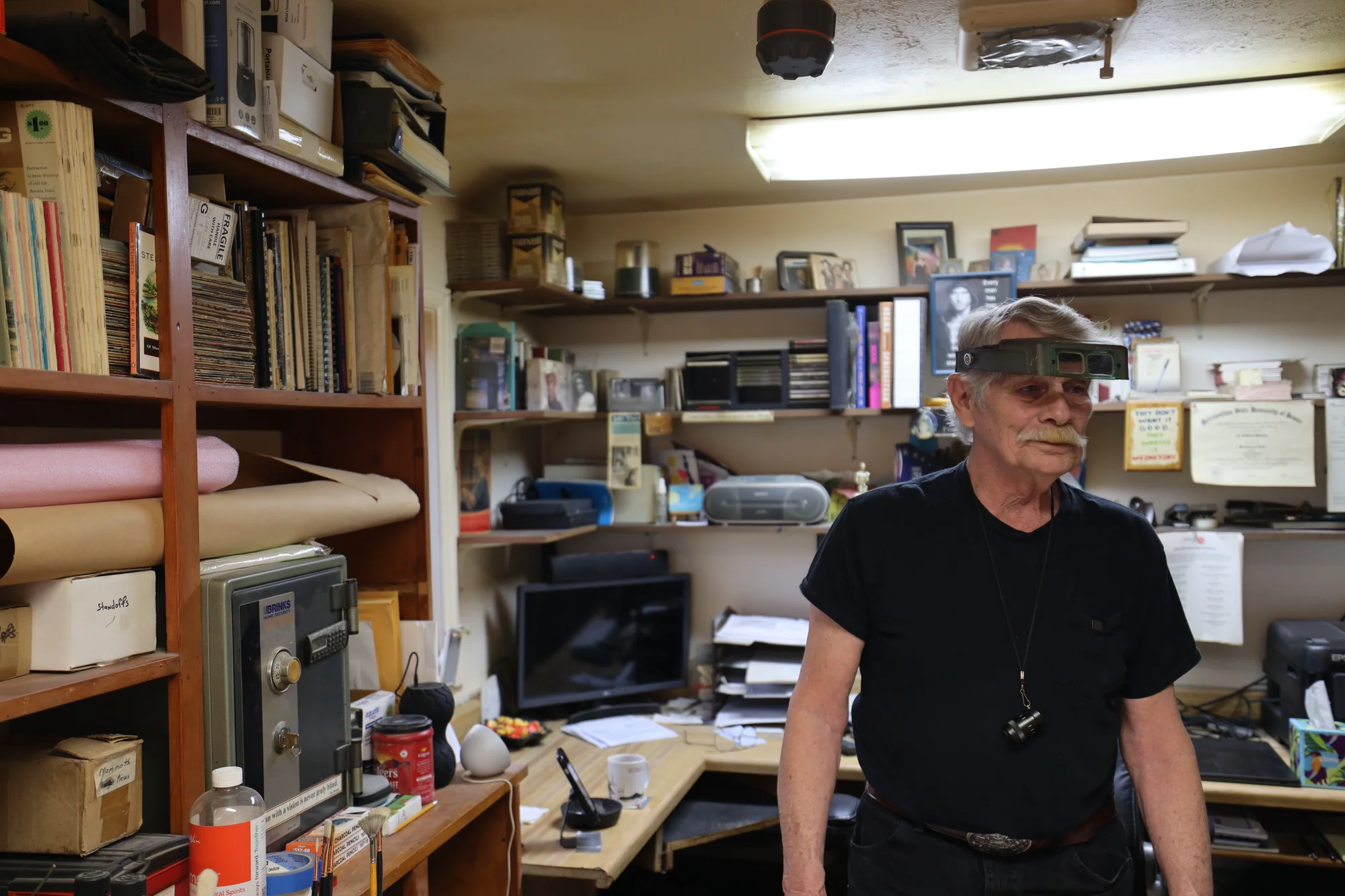 Jim Stevens in his home studio, complete with his magnifying glasses and minifying lens. These tools are crucial for Jim's process as they help fill  gaps in his vision. Photo: Sarah Shoen, Rocky Mountain PBS