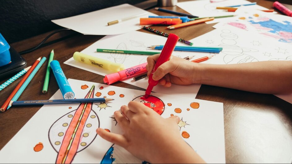A child's hand coloring pages on a table.
