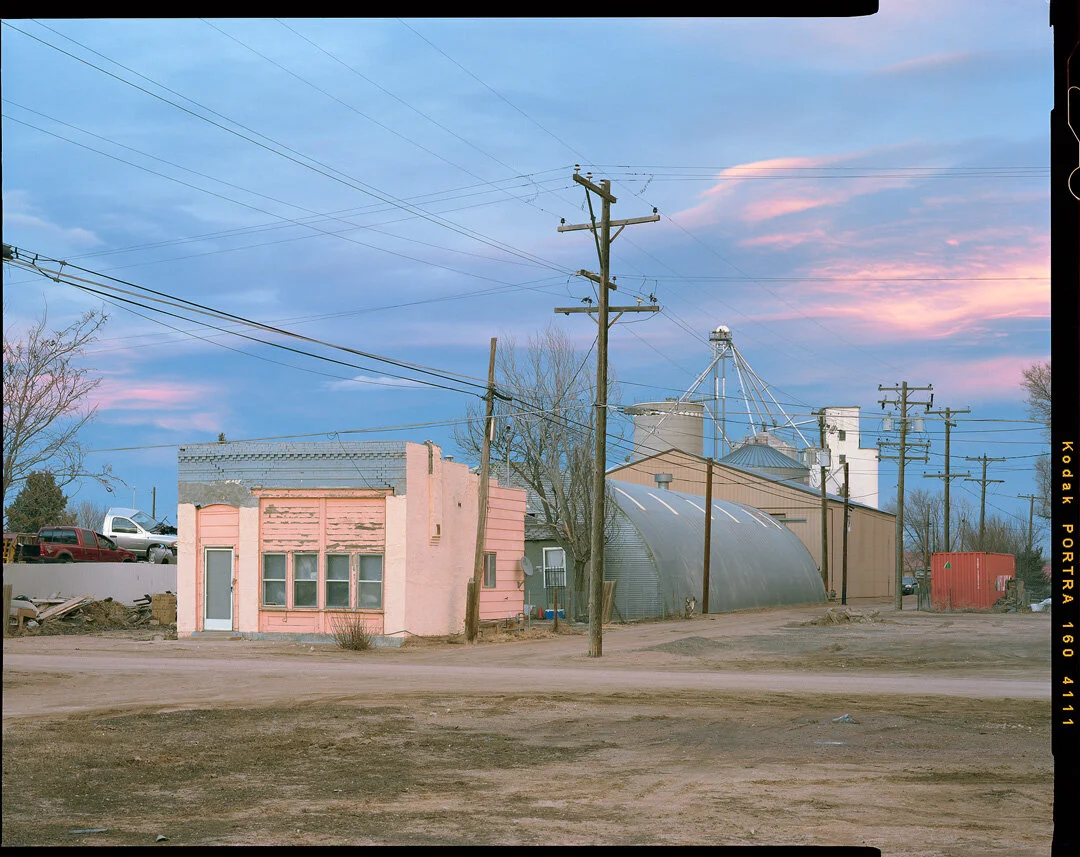 Trucks, old buildings, an empty lot and distant grain elevator, Weld County, March 2020. Photo courtesy Alex Burke