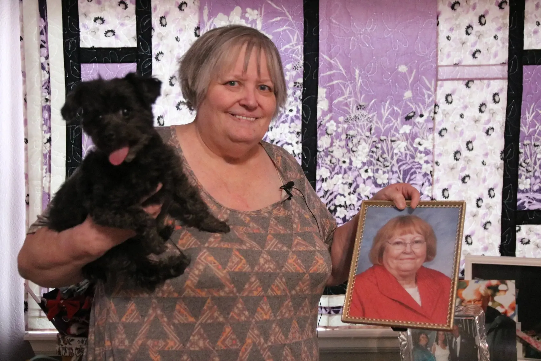 Lori Kratzer holds up a photo of her deceased mother, Shirley, in her bedroom on Nov. 21, 2025, in Arvada, Colo. When her mom bought the house, she asked Lori about what color she should paint the bathroom, showing her plan was for her daughter to move in after she passed. Photo: Emma VandenEinde, KUNC