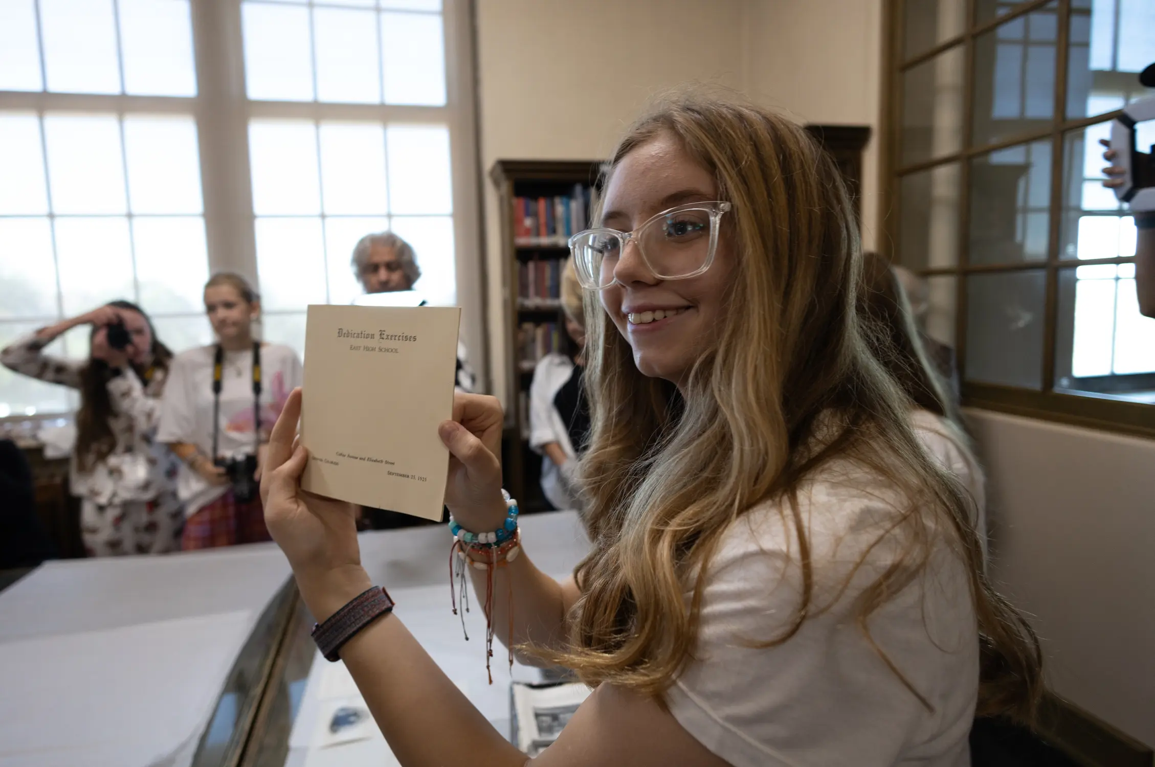 Marion Powers holds up a booklet of dedication exercises used at the original dedication ceremony of the current East High School building in 1925, found in one of the time capsules. Photo: Carly Rose, Rocky Mountain PBS.