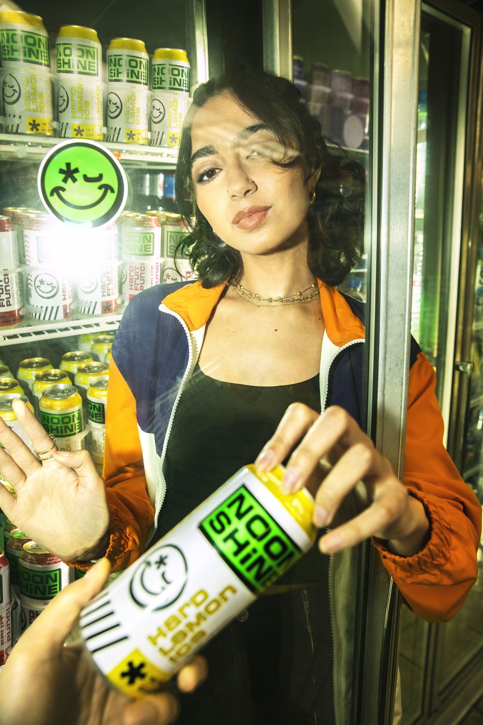 A girl handing a Noonshine Hard Lemonade Ice can from a fridge to another person (out of frame).